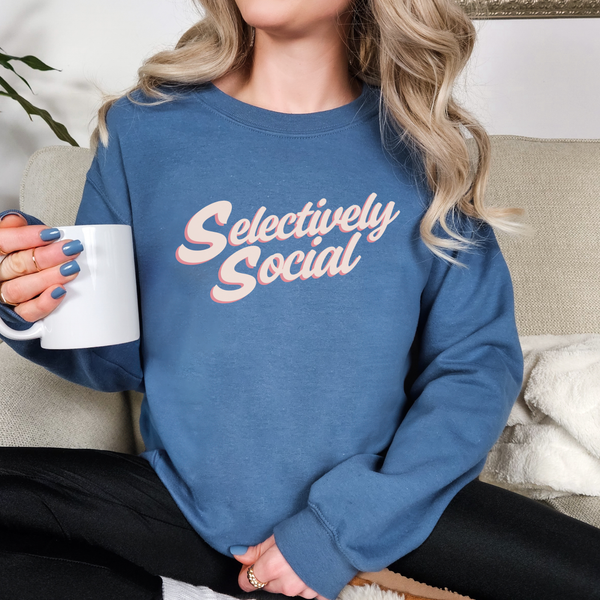 Woman sitting in a n indigo blue sweatshirt with the words "Selectively Social" written in a light pink script.