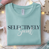 Folded light teal blue sweatshirt with 'SELECTIVELY Social' text on a soft surface with decorative elements.