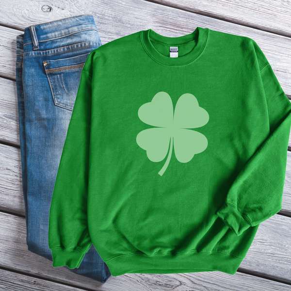 Green sweatshirt with a shamrock design on a wooden surface next to blue jeans.