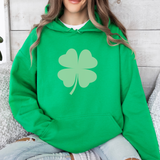 Woman wearing a green hoodie sweatshirt with a large lighter green shamrock in the middle.