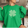 Woman wearing a green sweatshirt with a large lighter green shamrock in the middle.