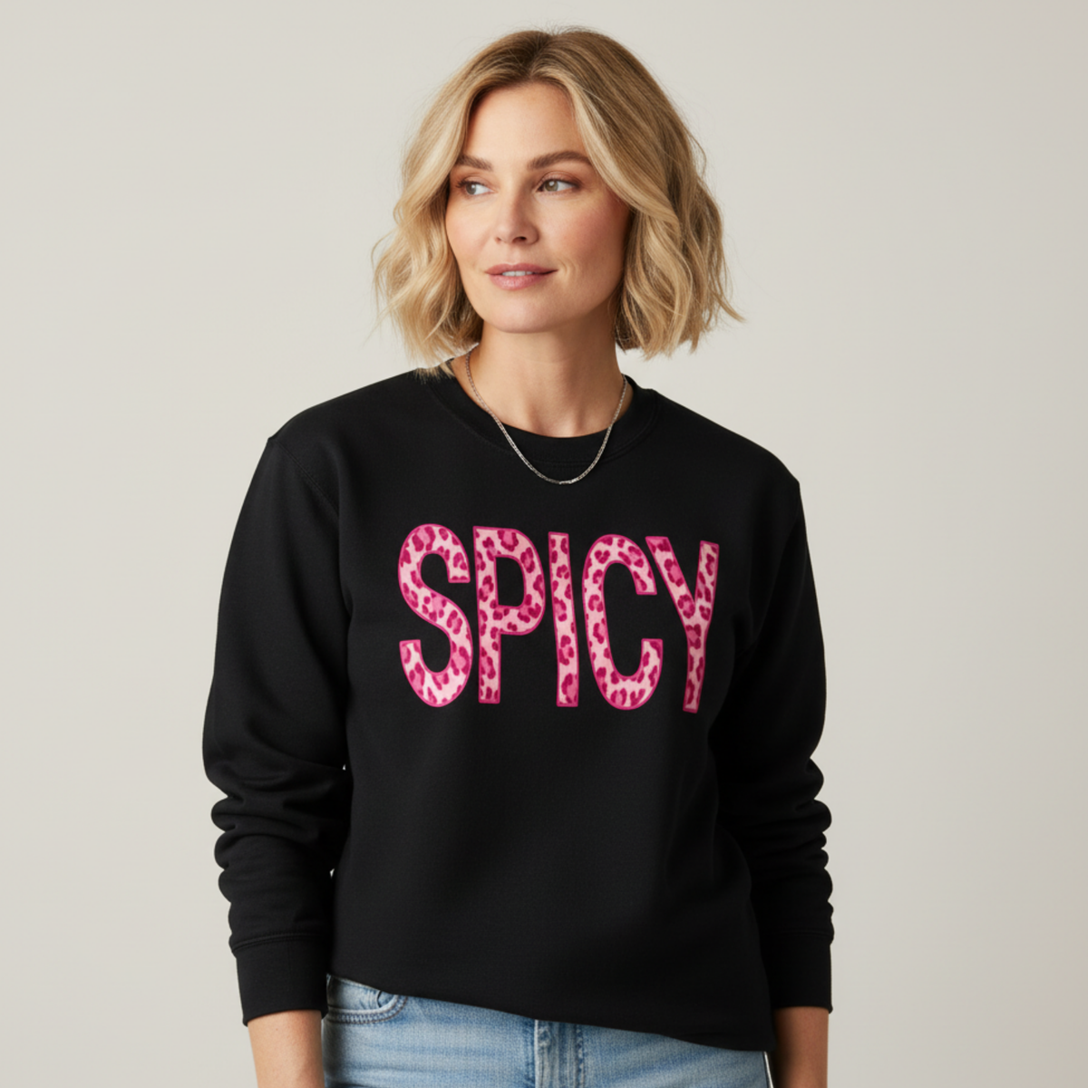 Woman wearing a black sweatshirt with 'SPICY' in pink leopard print on a plain background