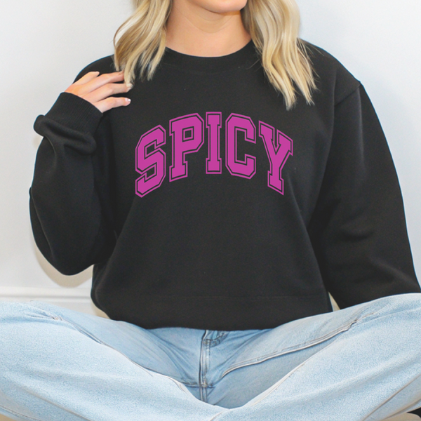 Person wearing a black sweatshirt with 'SPICY' in pink text, sitting on a white background.