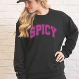 Person wearing a black sweatshirt with 'SPICY' in pink text against a light brick wall.