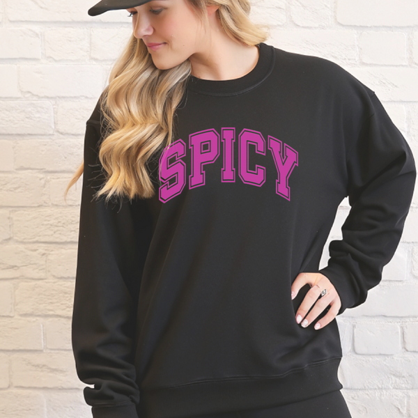 Person wearing a black sweatshirt with 'SPICY' in pink text against a light brick wall.