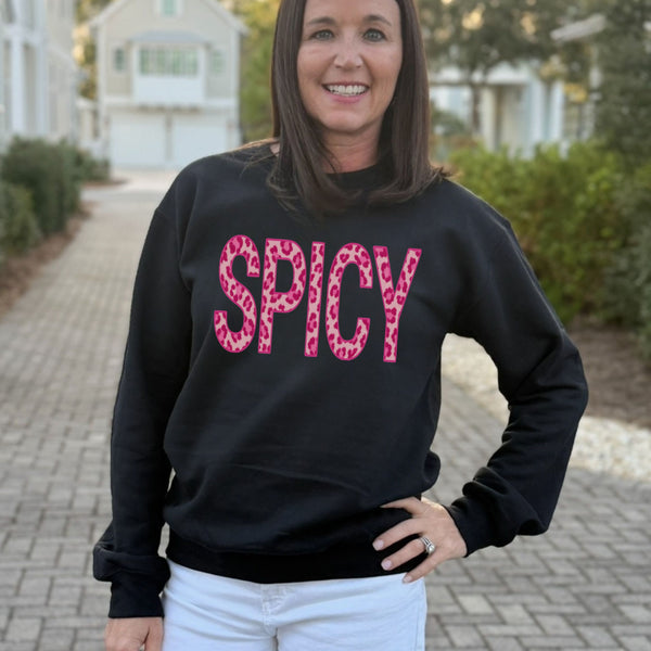 A woman wearing a black Spicy leopard print sweatshirt standing outdoors on a paved path.
