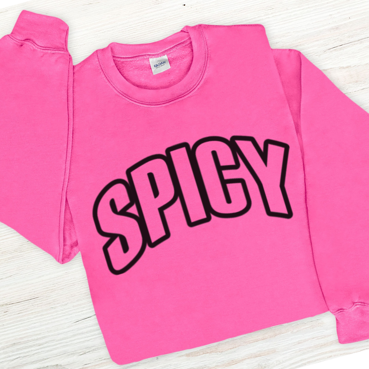 Pink sweatshirt with 'SPICY' text on a light wooden surface