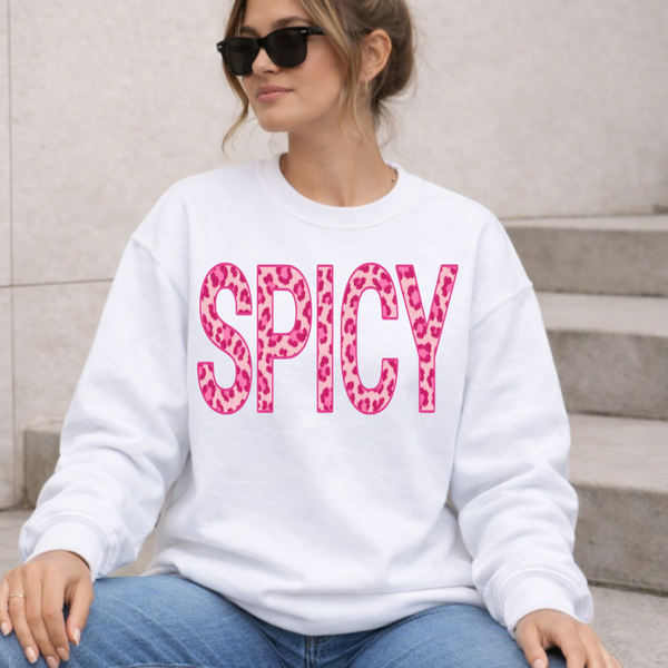 Woman wearing a white sweatshirt with 'SPICY' in pink leopard print text, sitting on steps.