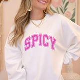 Person wearing a white sweatshirt with 'SPICY' in pink text, standing indoors.