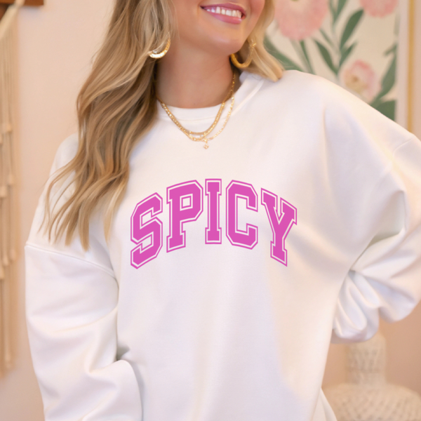 Person wearing a white sweatshirt with 'SPICY' in pink text, standing indoors.