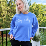 Woman wearing a blue sweatshirt with 'stay seated' text outdoors.