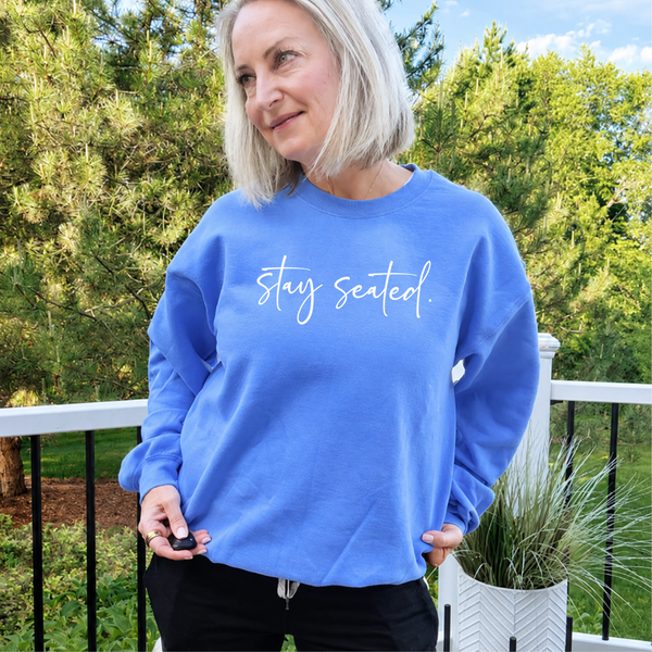 Woman wearing a blue sweatshirt with 'stay seated' text outdoors.