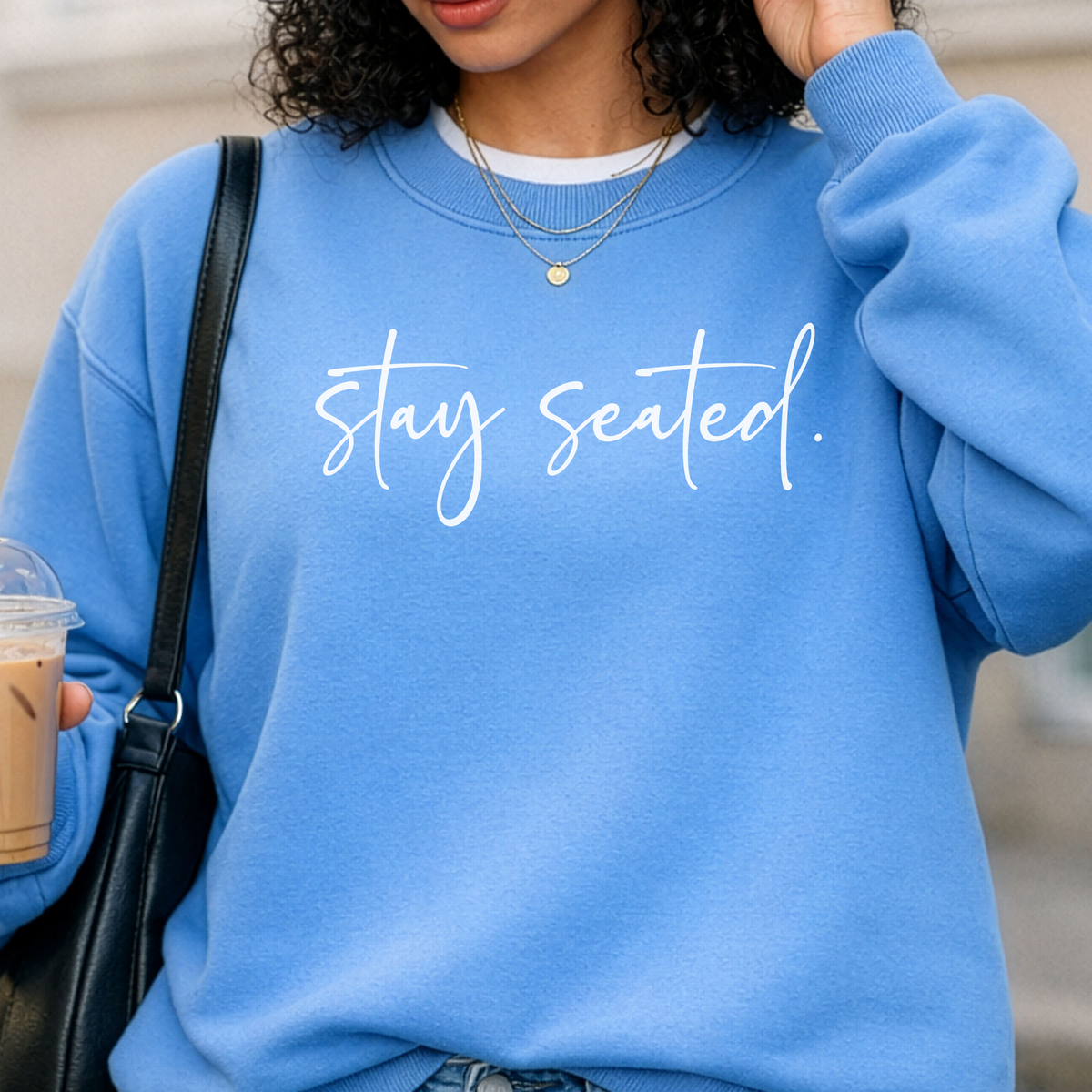 Person wearing a blue sweatshirt with 'stay seated' text, holding a coffee cup.