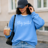Woman wearing a blue sweatshirt with 'stay seated' text, holding a drink.