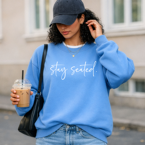 Woman wearing a blue sweatshirt with 'stay seated' text, holding a drink.
