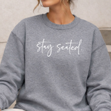 Gray sweatshirt with 'stay seated' text on a neutral background