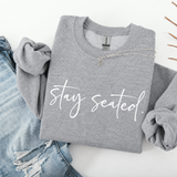 Folded gray sweatshirt with 'stay seated' text on a white background
