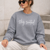 Woman wearing a gray sweatshirt with 'stay seated' text, sitting on steps.