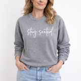 A woman wearing a gray sweatshirt with 'Stay Seated' text on a white background