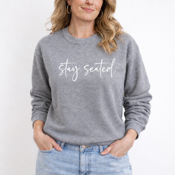 A woman wearing a gray sweatshirt with 'Stay Seated' text on a white background