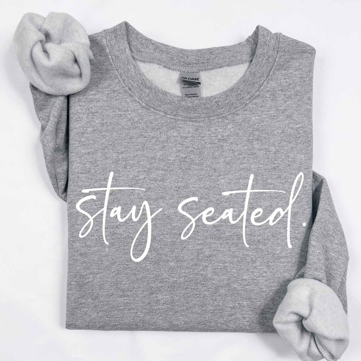 A darker heather gray folded sweatshirt on that says "Stay Seated" in a white script.