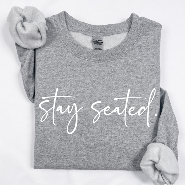 A darker heather gray folded sweatshirt on that says "Stay Seated" in a white script.