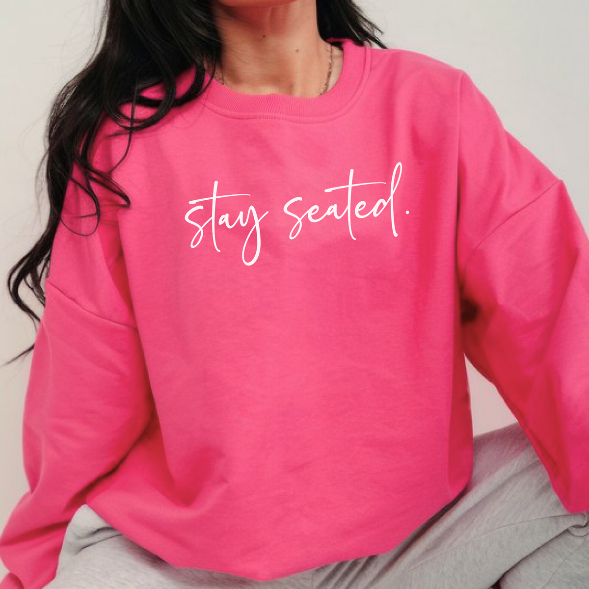 Person wearing a pink sweatshirt with 'stay seated' text on a plain background