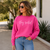 Woman wearing a pink sweatshirt with 'stay seated' text, standing outdoors.