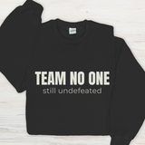 Black sweatshirt with 'TEAM NO ONE still undefeated' text on a light wooden surface