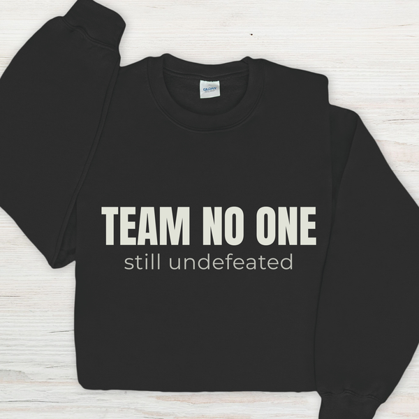 Black sweatshirt with 'TEAM NO ONE still undefeated' text on a light wooden surface