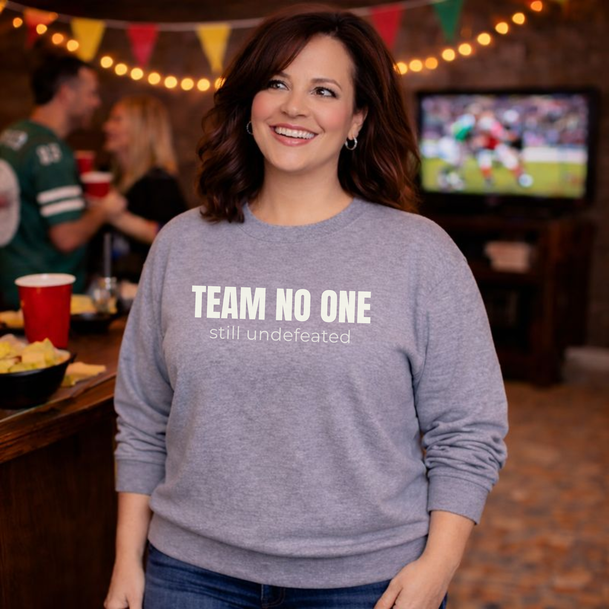 Woman wearing a gray sweatshirt with 'TEAM NO ONE still undefeated' text in a casual setting.