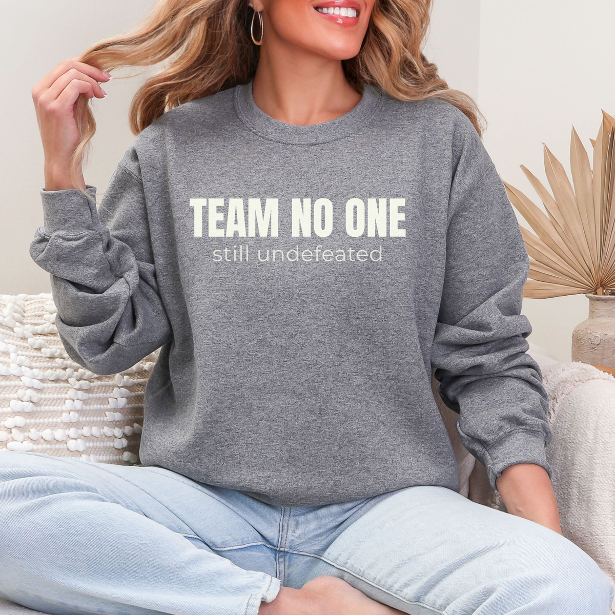 Person wearing a gray sweatshirt with 'TEAM NO ONE still undefeated' text, sitting on a couch.