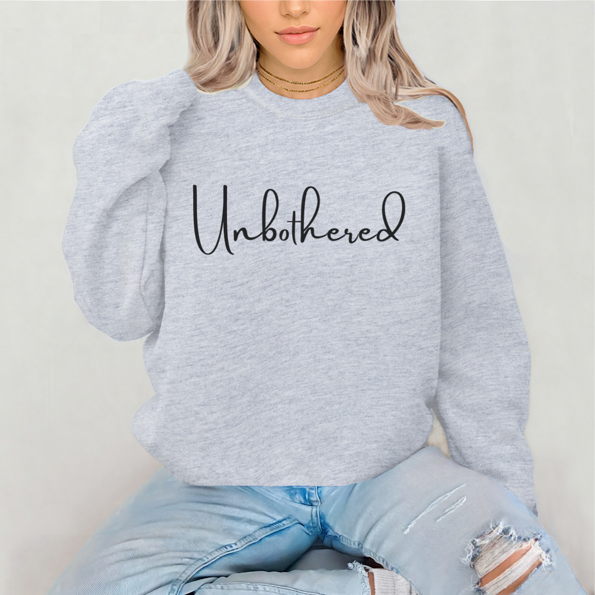 Woman wearing a gray sweatshirt with 'Unbothered' text on a plain background