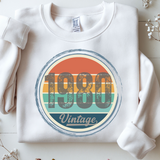 White sweatshirt with '1980 Vintage' design on a light wooden surface.