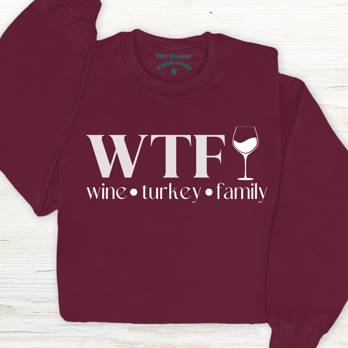 Maroon sweatshirt with 'WTF wine turkey family' text and wine glass graphic on a wooden surface