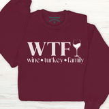 Maroon sweatshirt with 'WTF wine turkey family' text and wine glass graphic on a wooden surface