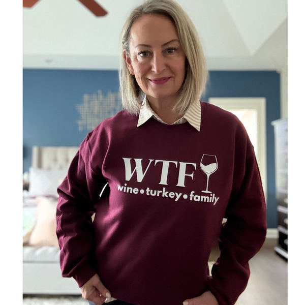 Woman wearing a maroon sweatshirt with 'WTF wine turkey family' text in a room.