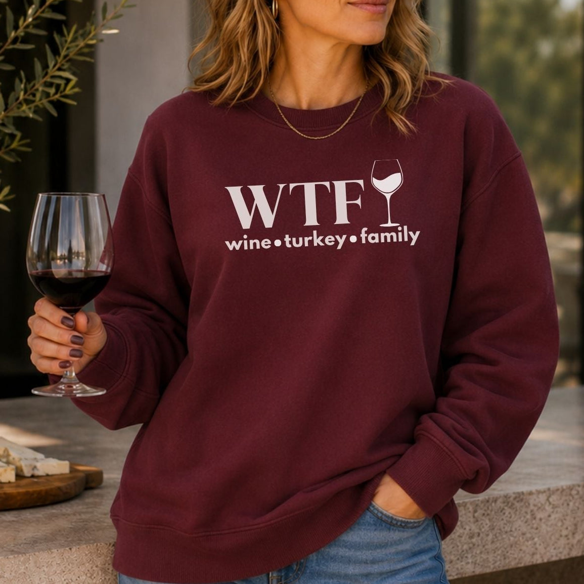 A woman holding a glass of wine wearing a sweatshirt that says "WTF Wine Turkey Family" with an outline of a wine glass.