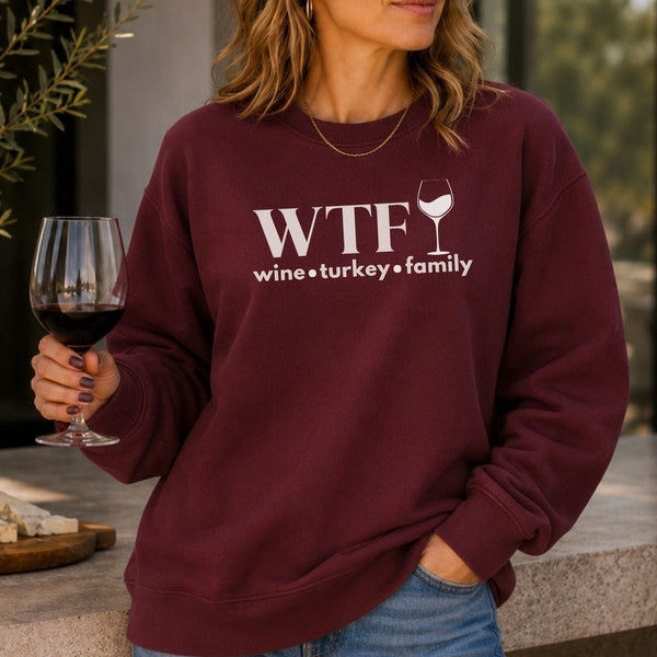 A woman holding a glass of wine wearing a sweatshirt that says "WTF Wine Turkey Family" with an outline of a wine glass.