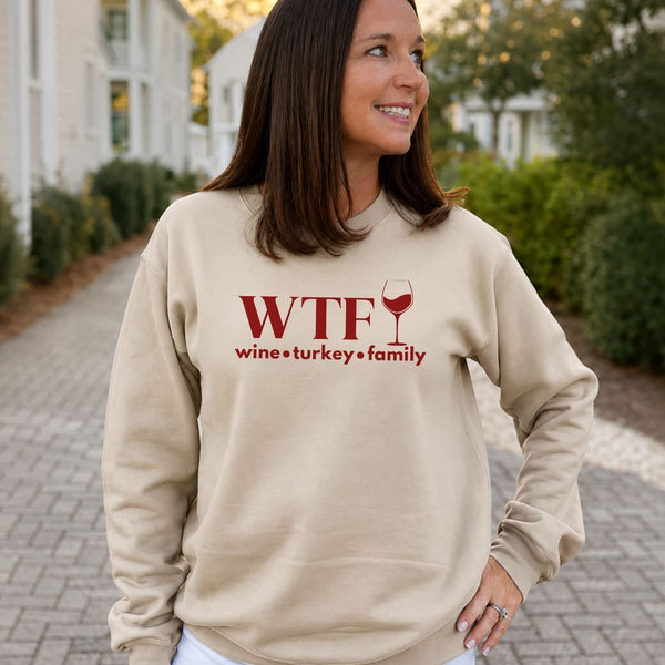 A woman standing outside in a sand beige sweatshirt that reads "WTF Wine Turkey Family" and an outline of a wine glass