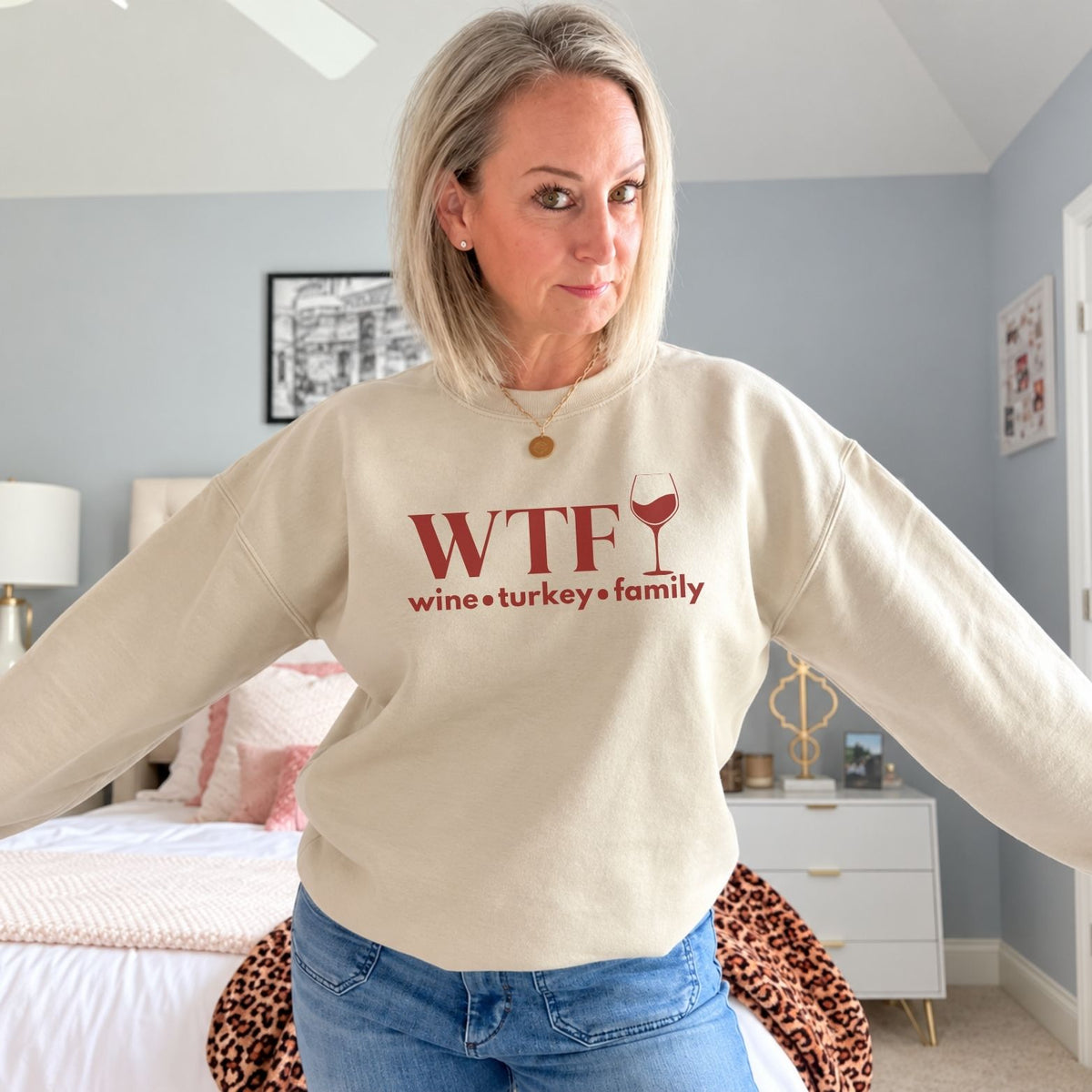 A woman standing in a sand beige sweatshirt that reads "WTF Wine Turkey Family" and an outline of a wine glass
