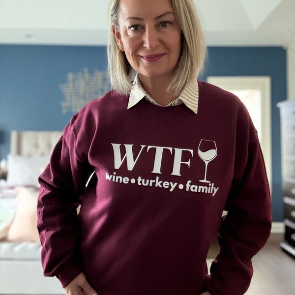 A woman standing in a maroon sweatshirt that reads "WTF Wine Turkey Family" and an outline of a wine glass