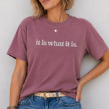 Person wearing a purple t-shirt with 'it is what it is' text against a white background