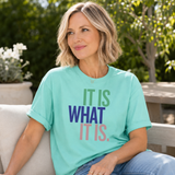 Woman wearing a light blue t-shirt with text sitting outdoors.