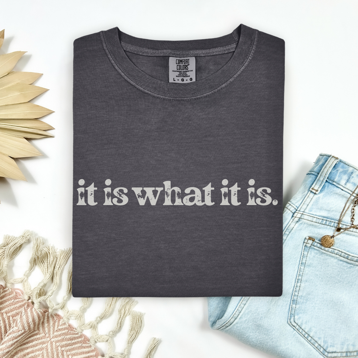 Dark gray t-shirt with 'it is what it is' text on a white background with decorative elements.
