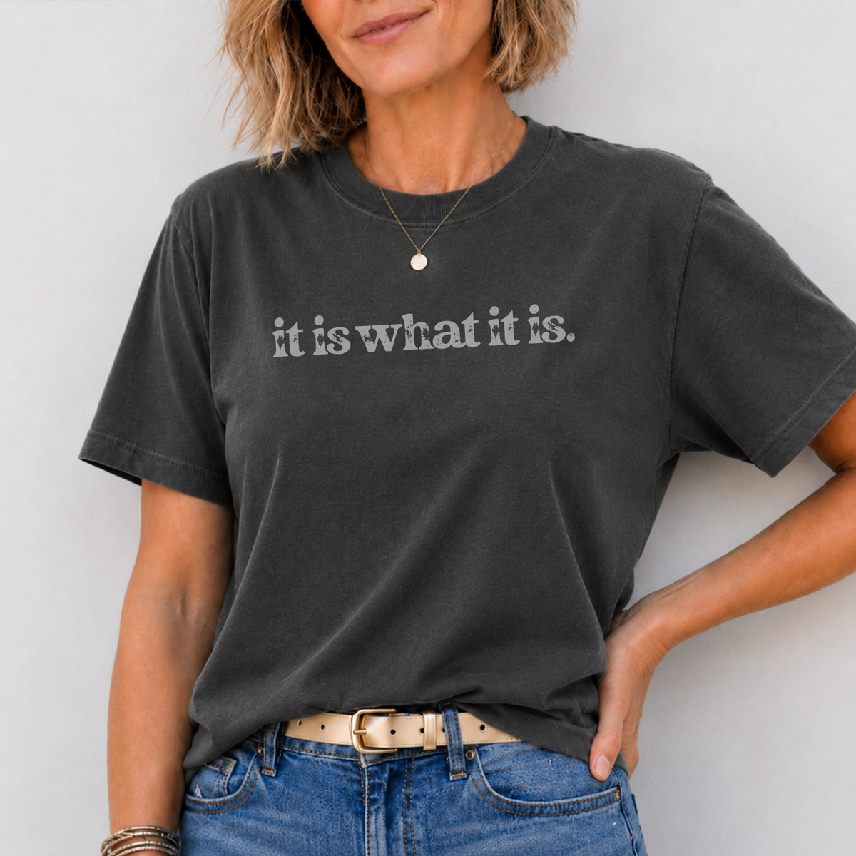 Person wearing a black t-shirt with 'it is what it is' text against a light background