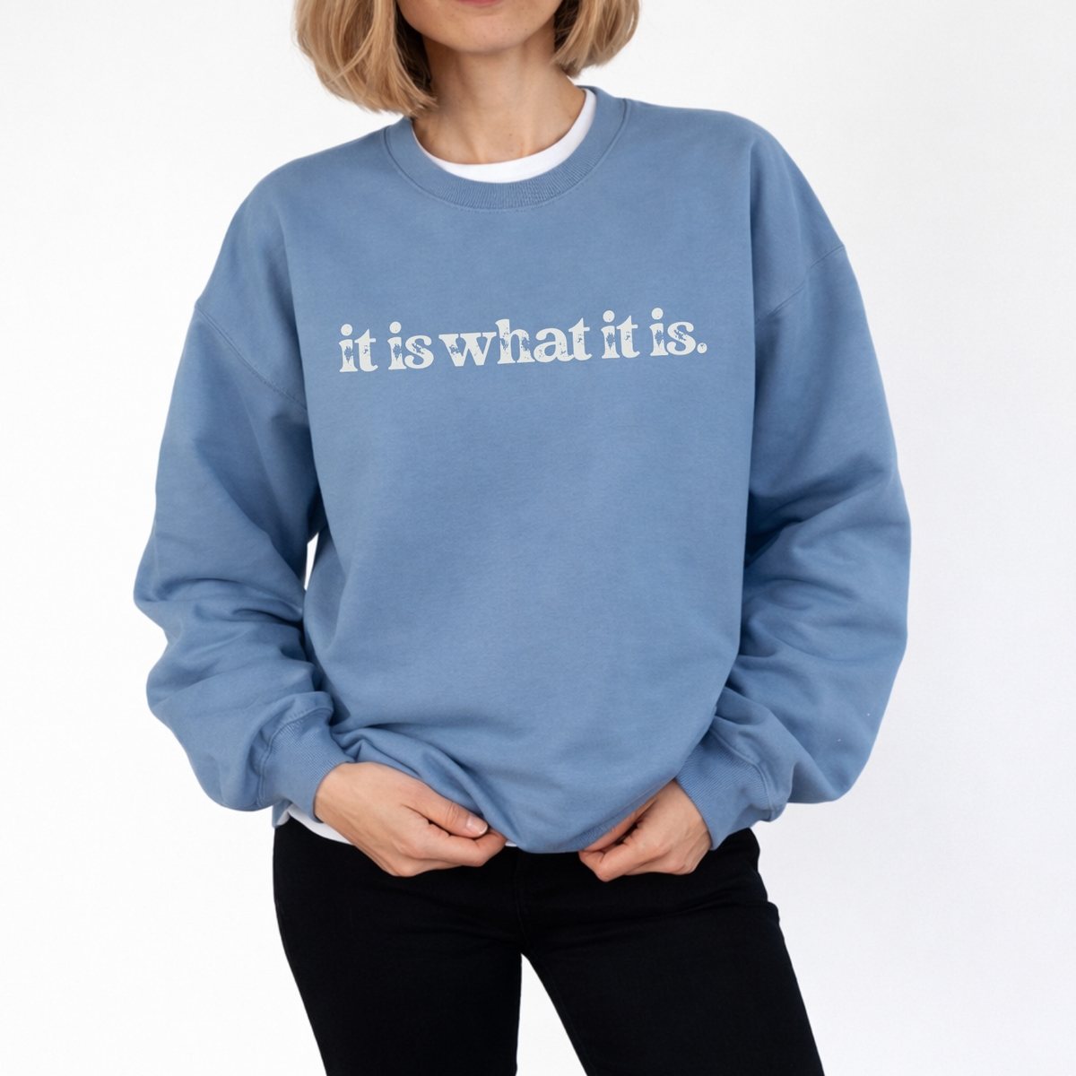 A woman wearing a blue sweatshirt with "It is what it is" text on a white background