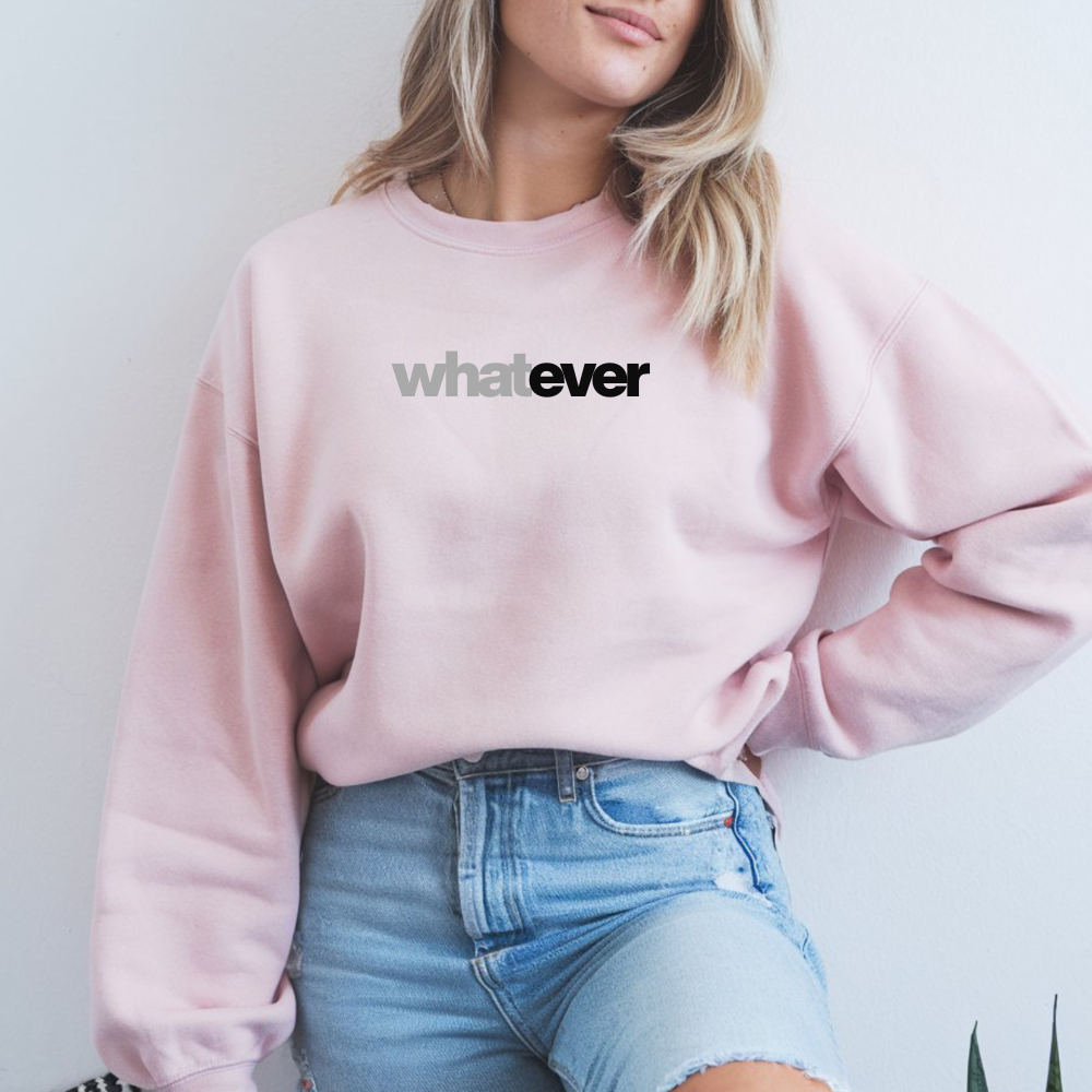 A woman wearing a pink sweatshirt with 'whatever' text and blue jeans against a white background