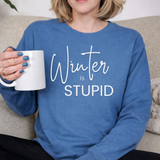 A woman  wearing a blue sweatshirt with 'Winter is STUPID' text, holding a white mug.