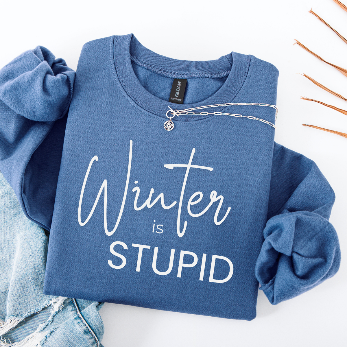 A Blue folded sweatshirt with 'Winter is Stupid' text on a white background
